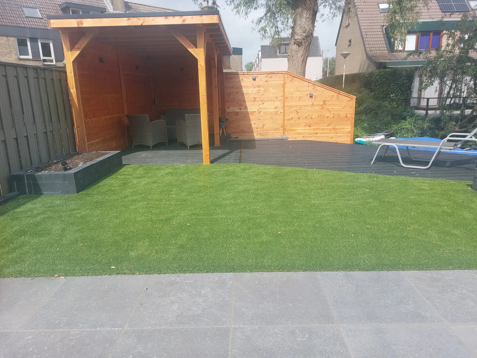 Kunstgras voor een houten overkapping met bijpassende schutting en loungehoek