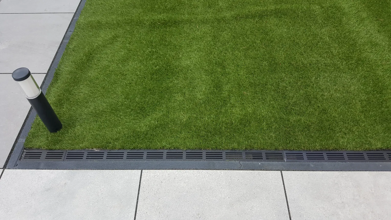 Kunstgras strak aangesloten op lichte keramische terrastegels met lijngoot en tuinspot