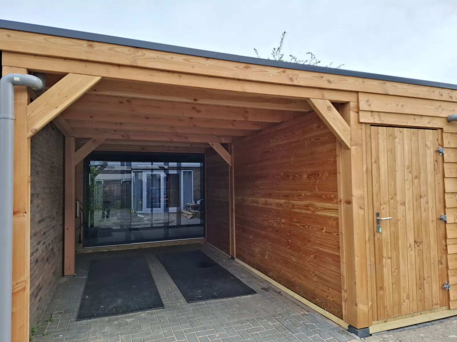 Overkapping met berging en doorkijk door glazen wanden naar de woning