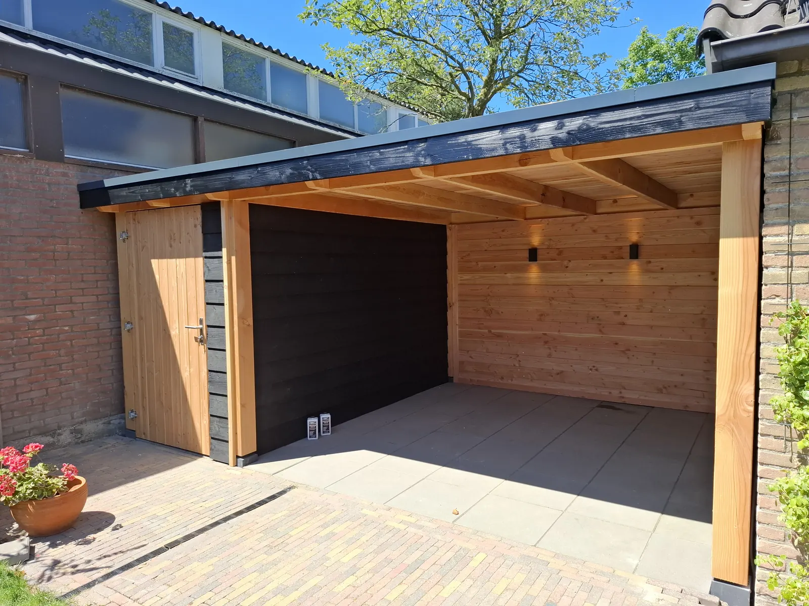 Houten overkapping aan de gevel met zwarte achterwand en wandverlichting