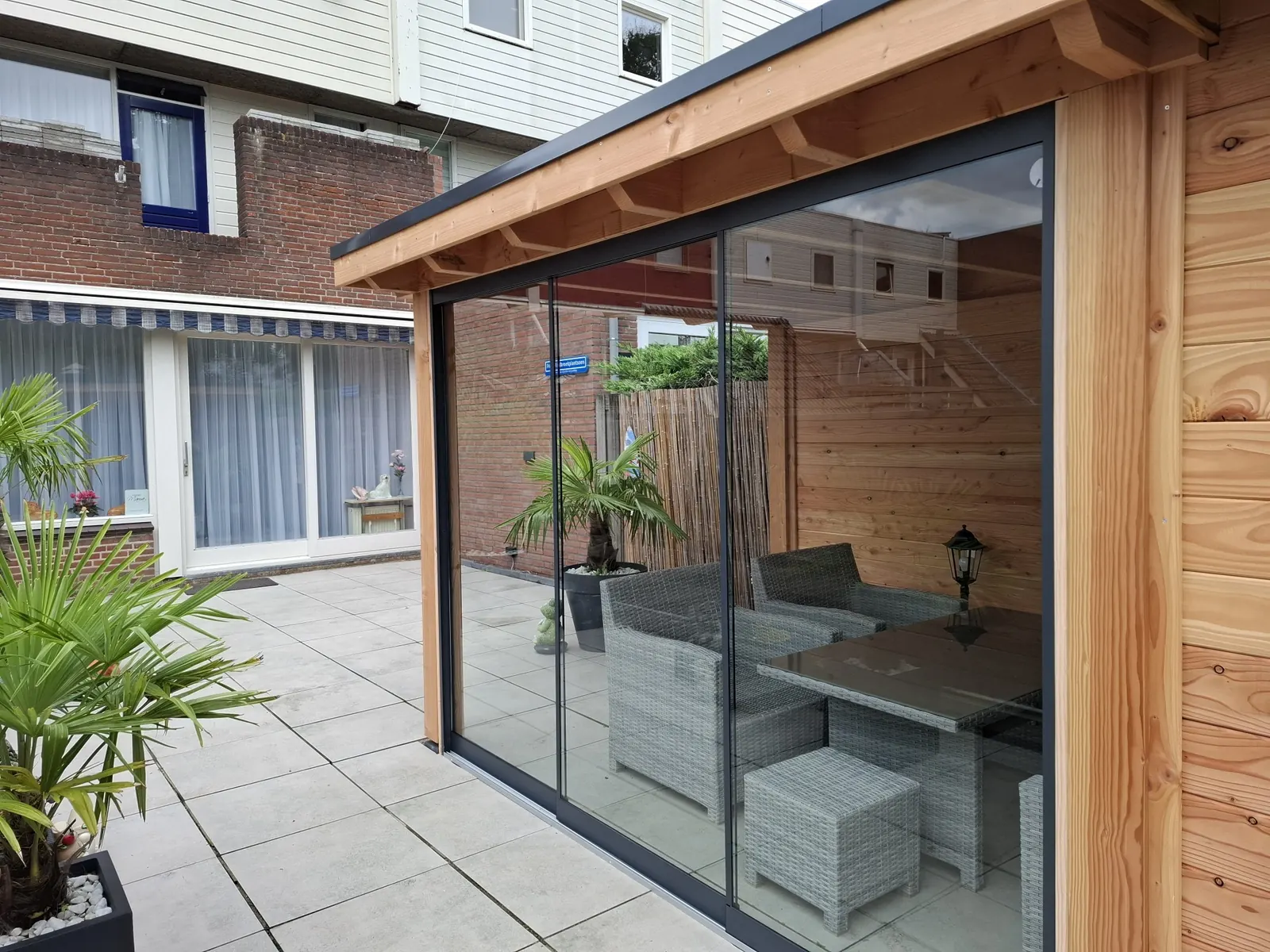 Houten overkapping met glazen schuifwanden op een terras van grote tegels