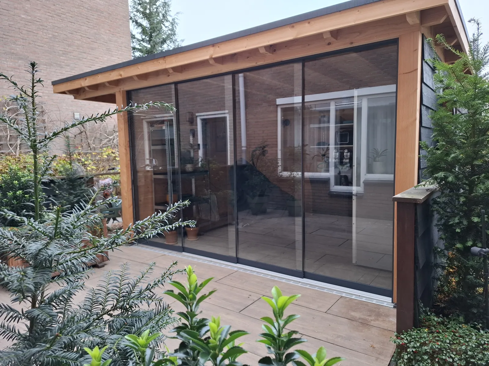 Overkapping met glazen schuifwanden tussen het groen van een stadstuin