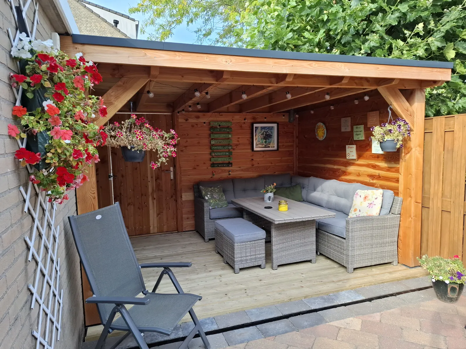 Houten overkapping met loungeset, hangende bloembakken en sfeerlampjes