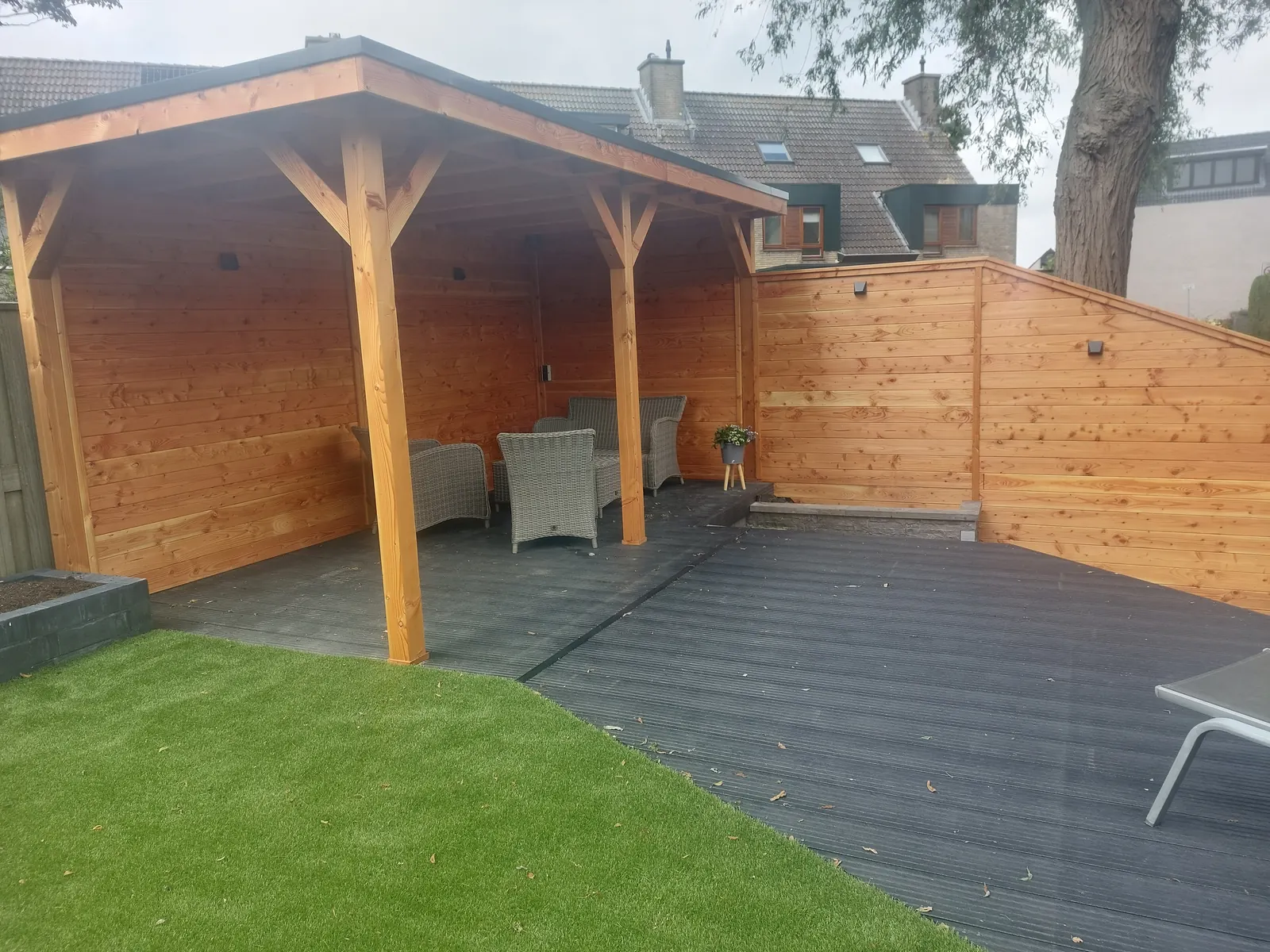 Houten overkapping met schutting, loungeset en vlonder, omringd door kunstgras