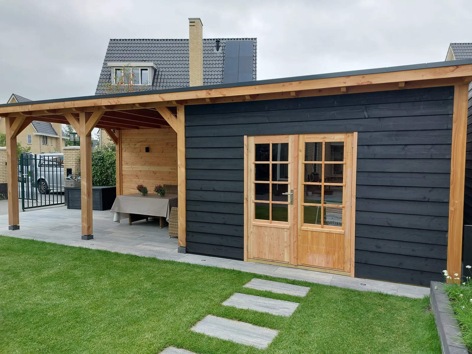 Tuinhuis van zwart gebeitst hout met aangebouwde douglas overkapping en openslaande deuren