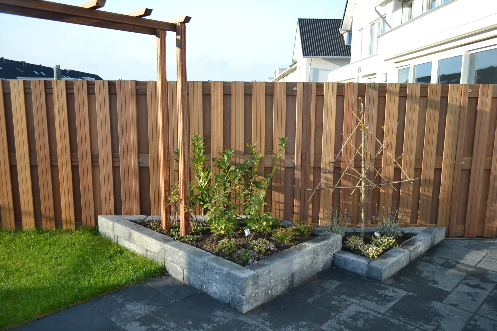 Verhoogde plantenbakken van stapelblokken voor een houten schutting met pergola