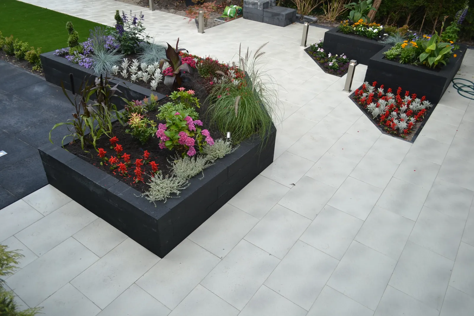 Zwarte plantenbakken met vaste planten op lichte terrastegels