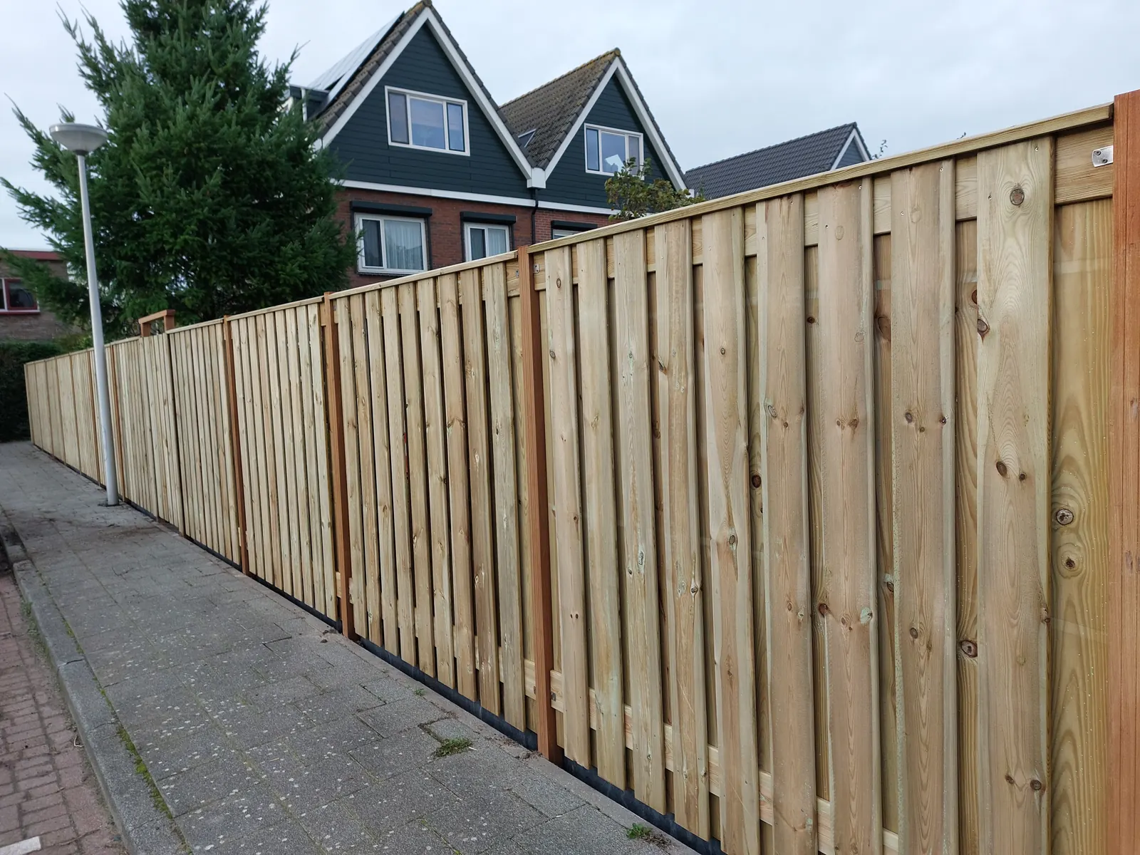 Lange houten schutting langs het trottoir bij een hoekwoning