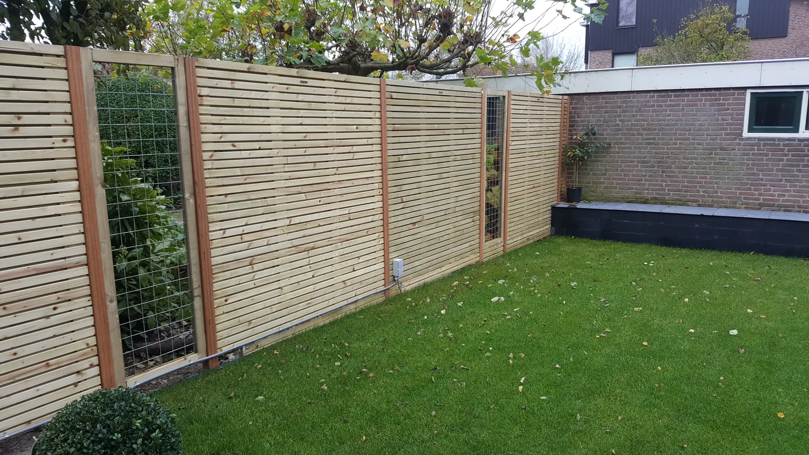 Houten schutting met gaaspanelen langs een gazon