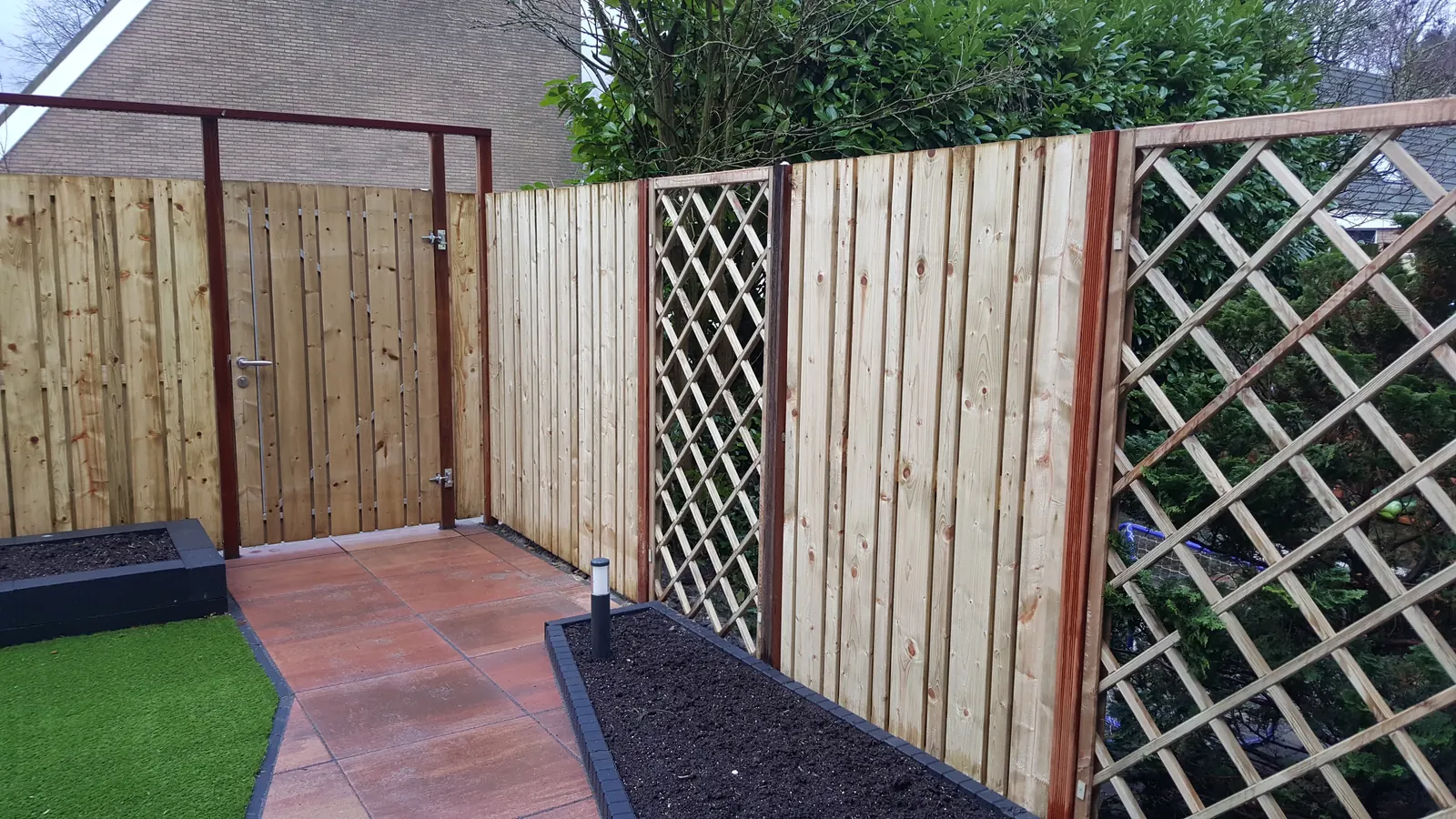 Houten schutting met tuinpoort en trellis naast een tuinpad
