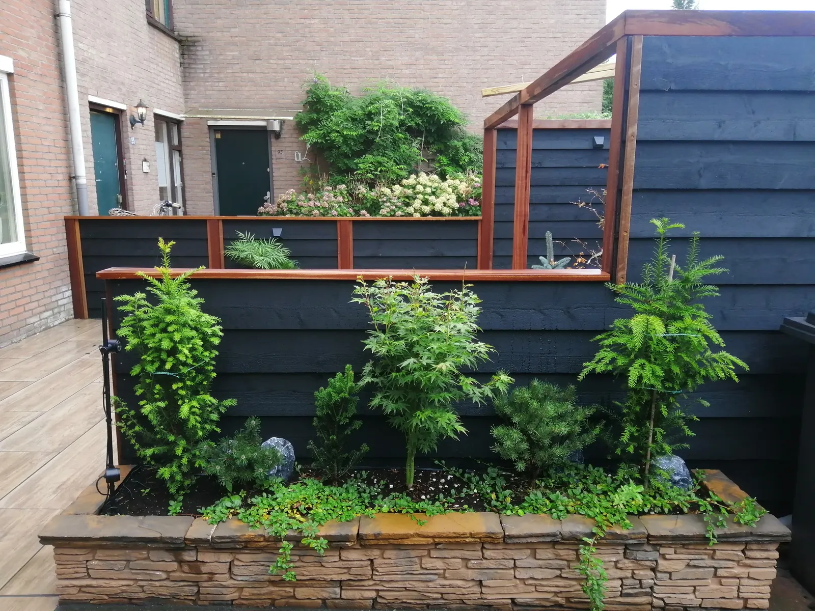 Zwart gebeitste schutting met een plantenbak van natuursteen