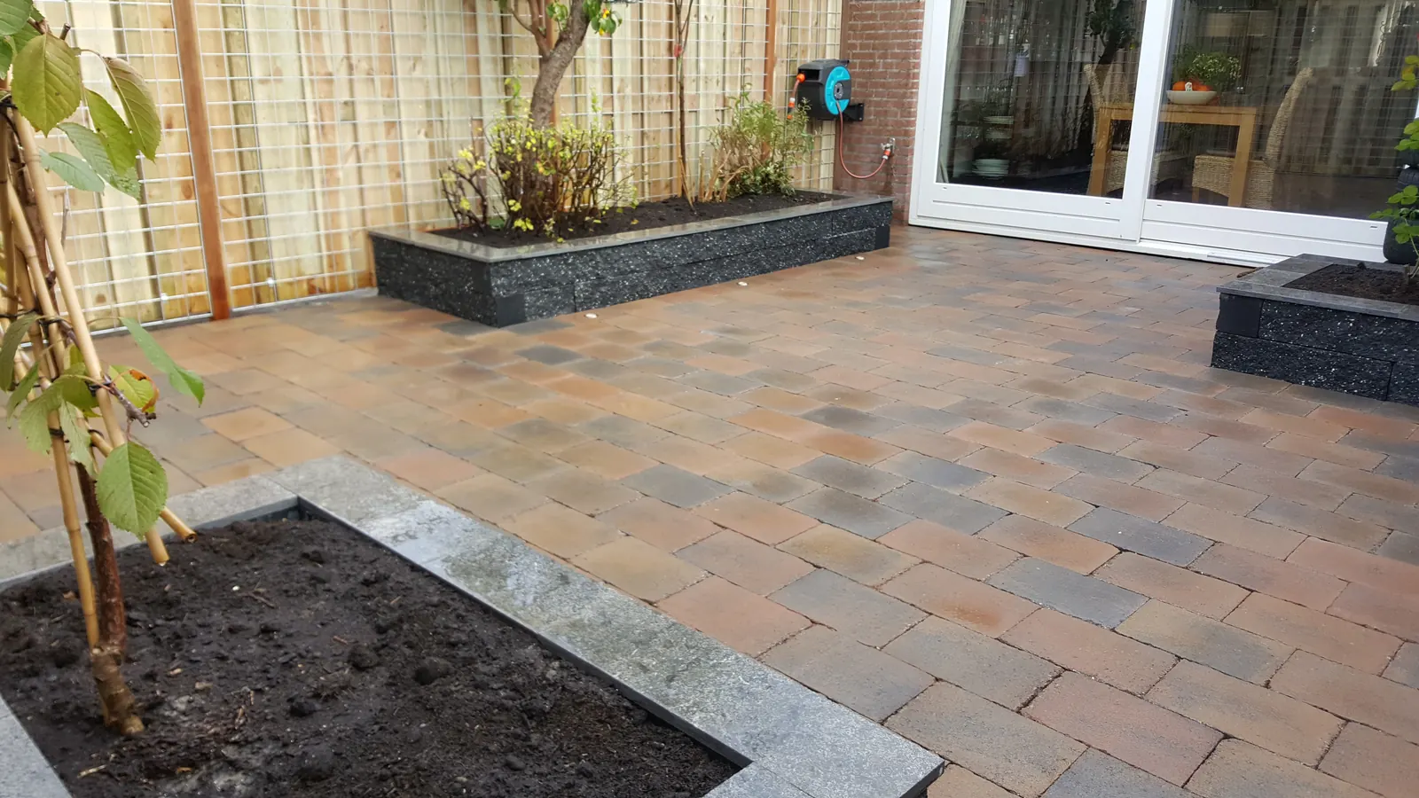 Terras van gebakken klinkers met een verhoogde plantenbak en jonge boom