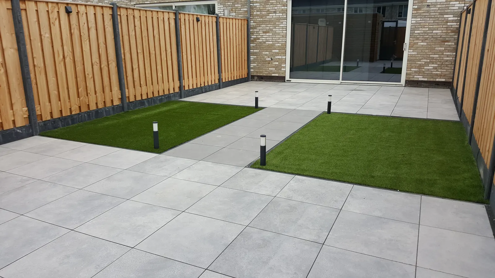 Terras van grote grijze tegels met kunstgras en een houten schutting