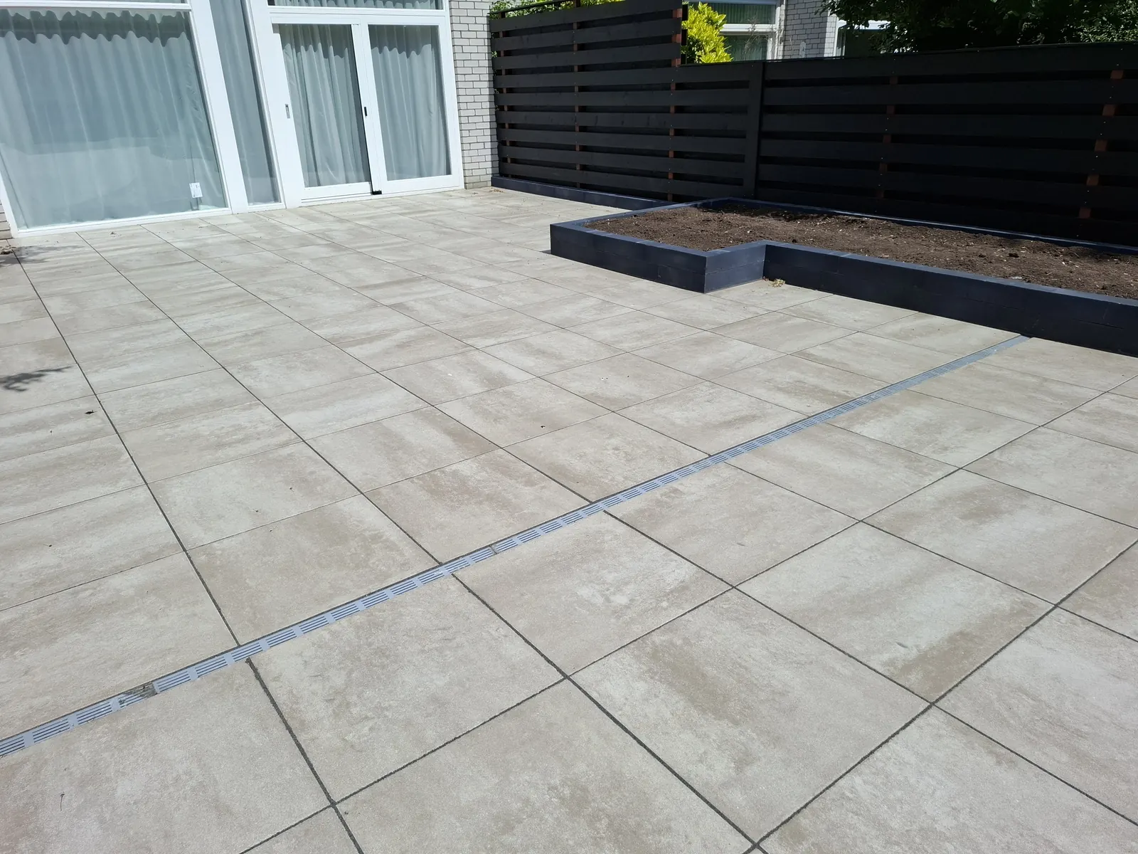 Terras van grote tegels met lijngoot en verhoogde plantenbak