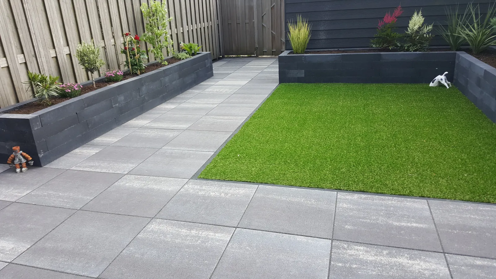 Terras met kunstgras en een antraciet plantenbak langs de schutting
