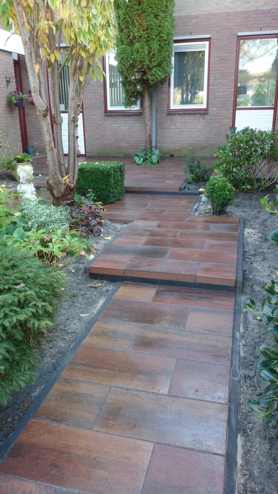 Tuinpad van roodbruine tegels tussen de beplanting
