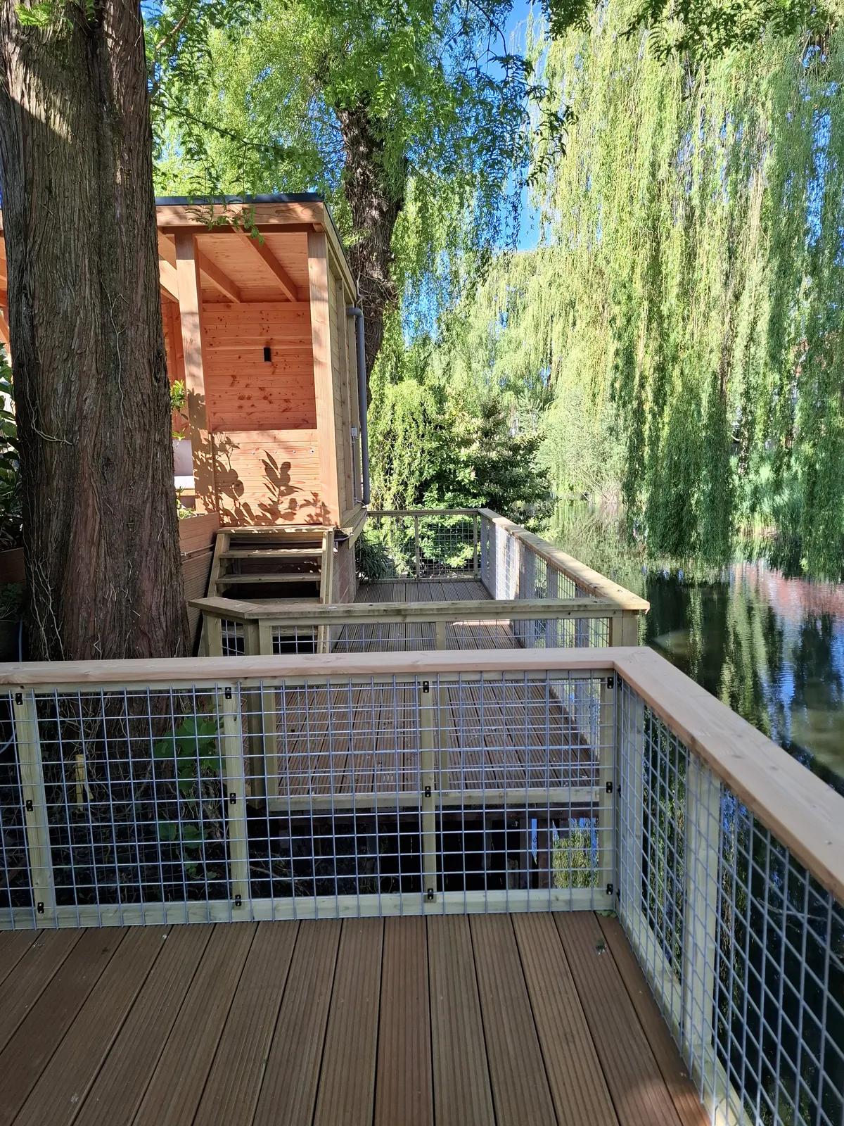 Vlonder met houten balustrade onder een treurwilg