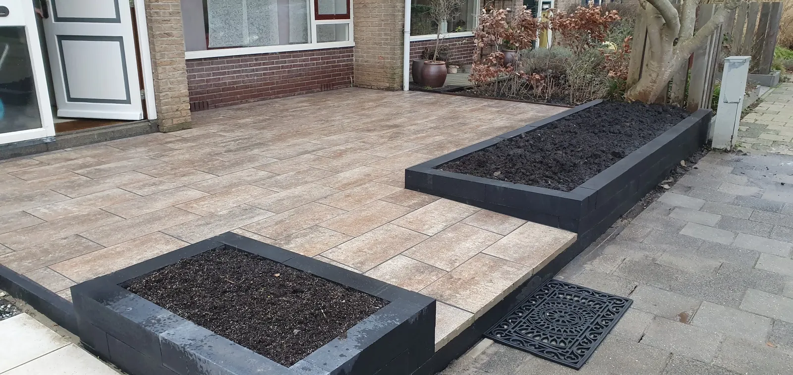 Voortuin met houtlook tegels en zwarte plantenbakken