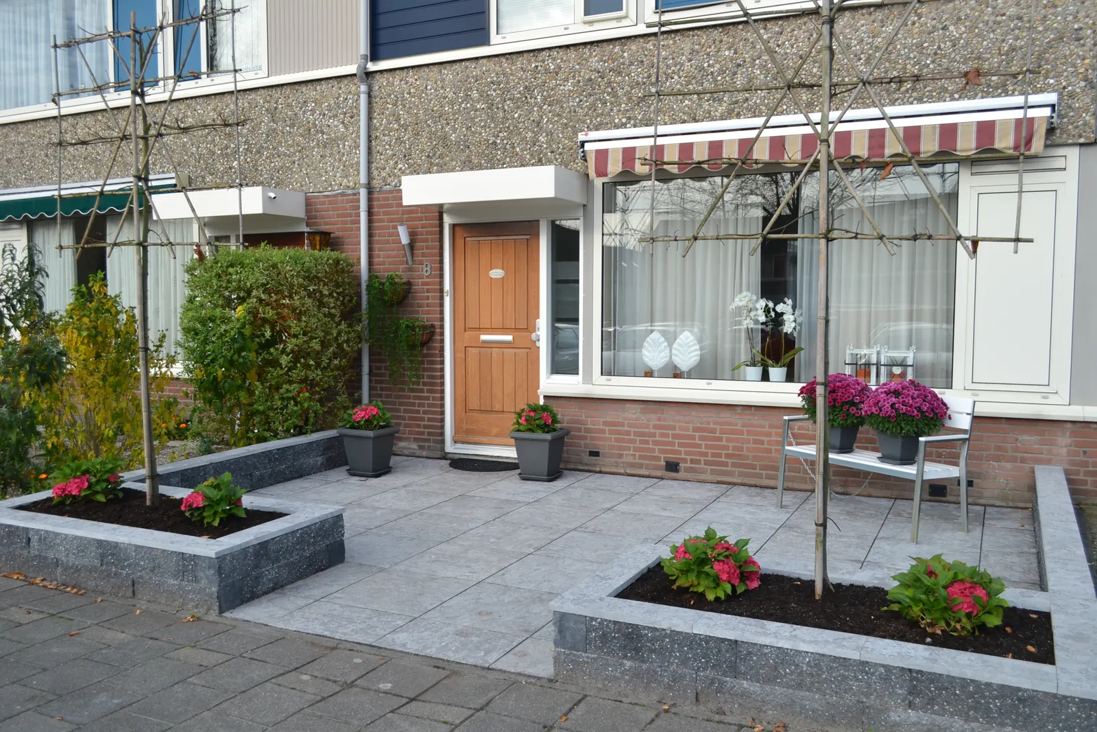 Voortuin met grijze tegels en verhoogde plantvakken voor de woning