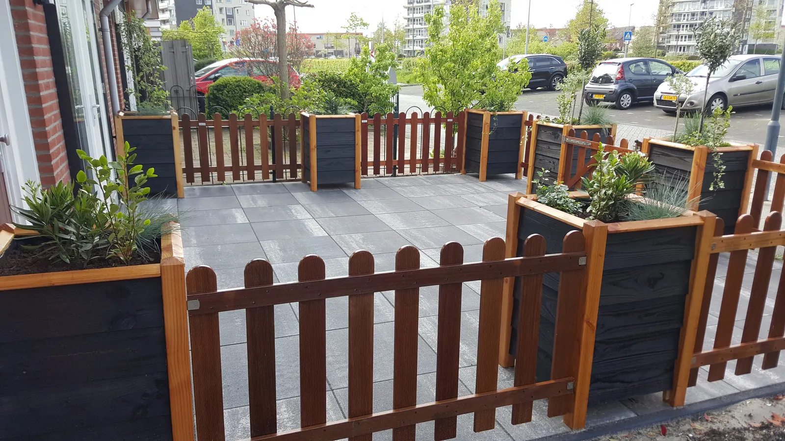 Voortuin met zwarte plantenbakken en een laag houten hekwerk